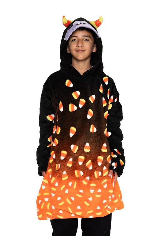 A child smiles against a plain white background wearing Fang the Monster Hooded Blanket, a black and orange hooded blanket with candy corn patterns and attached plush devil horns.