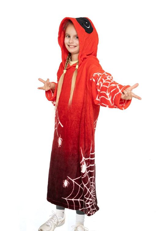A smiling young girl wears the Muffet the Spider Hooded Blanket, covered in white spider webs and cartoon spiders, standing with arms outstretched and making a playful hand gesture.