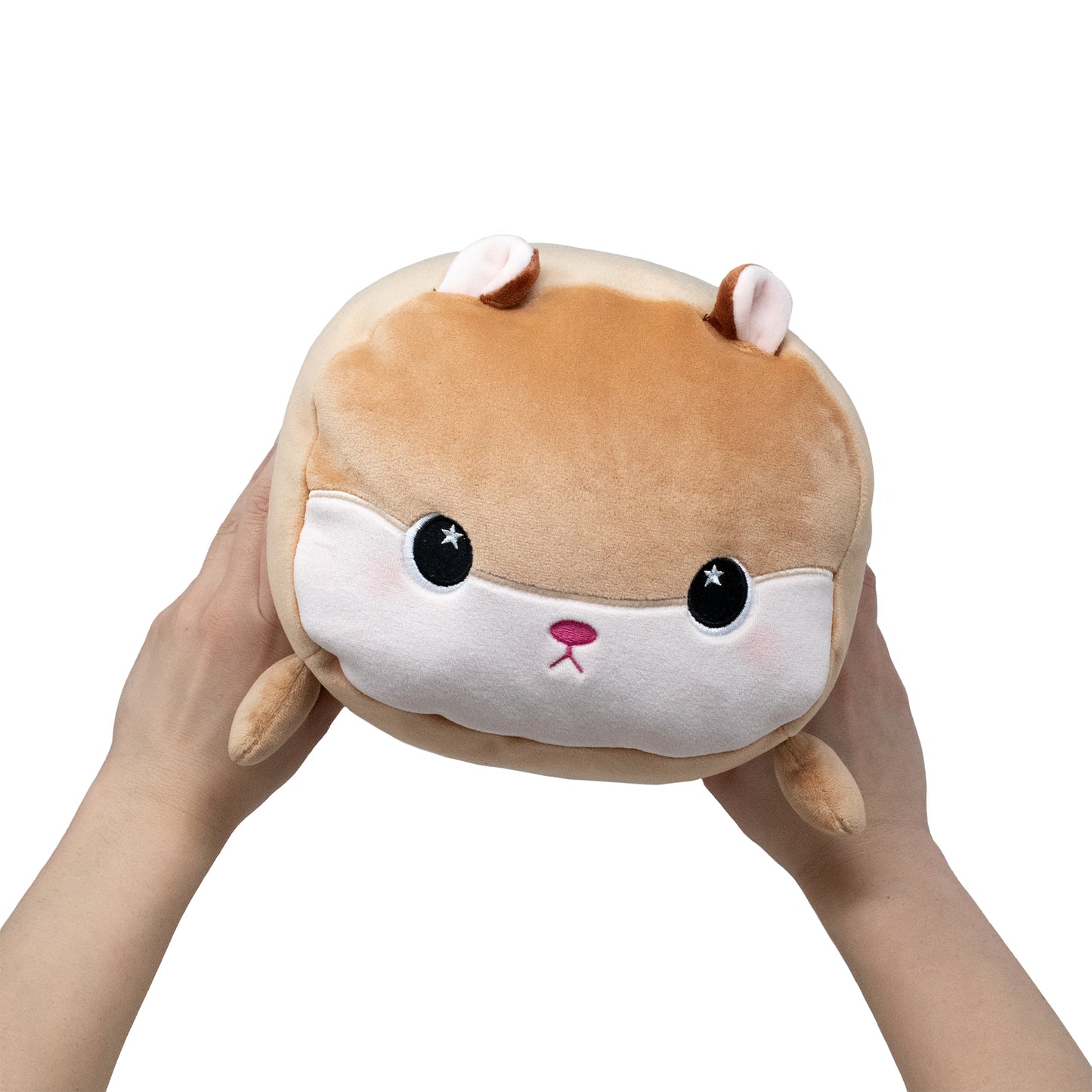 A pair of hands holds Hammy the Hamster, a round brown and white plush toy with large black eyes, small ears, and a cute pink nose, against a plain white background.