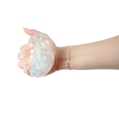 A hand squeezes Bubblegum's Favorite Toy - Mystery Dumpling, a translucent, iridescent stress relief squishy, against a white background. The toy glimmers as the person wearing a delicate bracelet gently presses it.