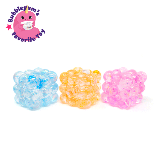 Three translucent Glitter Bubble Cubes in blue, yellow, and pink sit on a white background. In the top left corner, a pink cartoon mascot appears alongside the text “Bubblegum’s Favorite Toy – Glitter Bubble Cube.”.