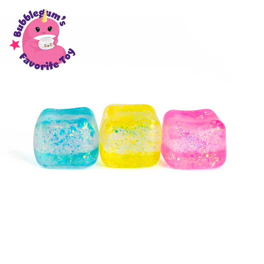 Three translucent Glitter Sugah-mals Cubes from Bubblegum's Favorite Toy in blue, yellow, and pink are lined up on a white background. A pink cartoon character appears with the text “Bubblegum’s Favorite Squishy Toy” for stress relief.