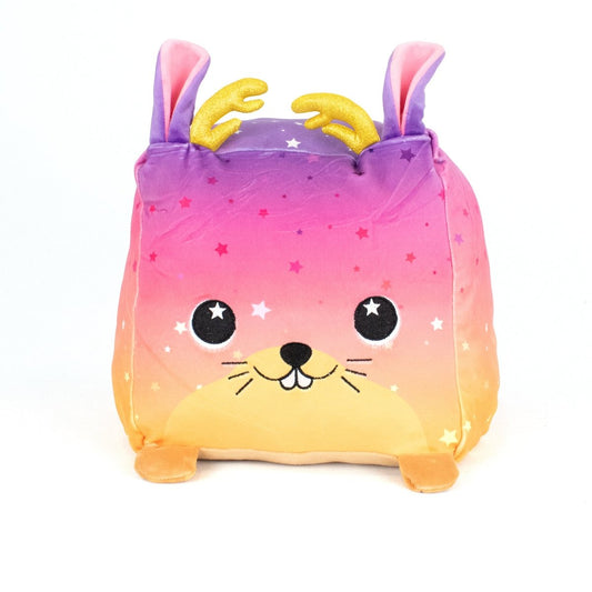 Jinx the Jackalope is a square, machine washable plush toy with a gradient pink, purple, and yellow body, star patterns, smiling face, rabbit ears, golden antlers, and small feet—perfect for plush fans. Pictured on a white background.