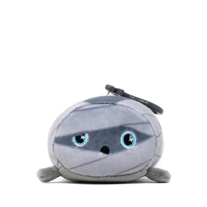 Nile the Mummy Clip-On is a round, gray plush toy with blue eyes and a keychain attachment. This soft and cute stuffed animal boasts a friendly expression and a simple, cartoonish design that adds charm to any collection.