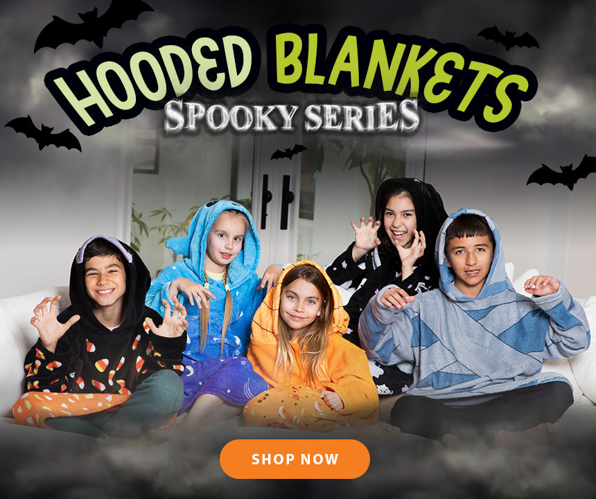 Children wearing hooded blankets with a Halloween theme, sitting on a couch.