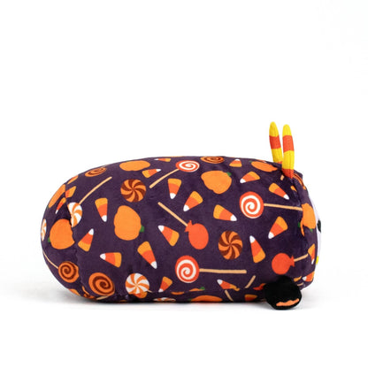 The Fang Spooky Slumber Plushie is a long oval plush toy made with ultra-soft purple fabric featuring orange pumpkins, candy corn, and lollipops. It has small yellow-orange horns, tiny black feet, and is machine washable for easy care.