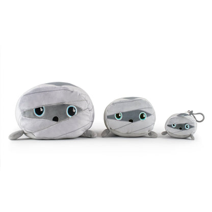 Nile the Mummy Plushies, arranged from largest to smallest, feature soft gray fabric and large round eyes for a friendly look. The smallest has a keychain.
