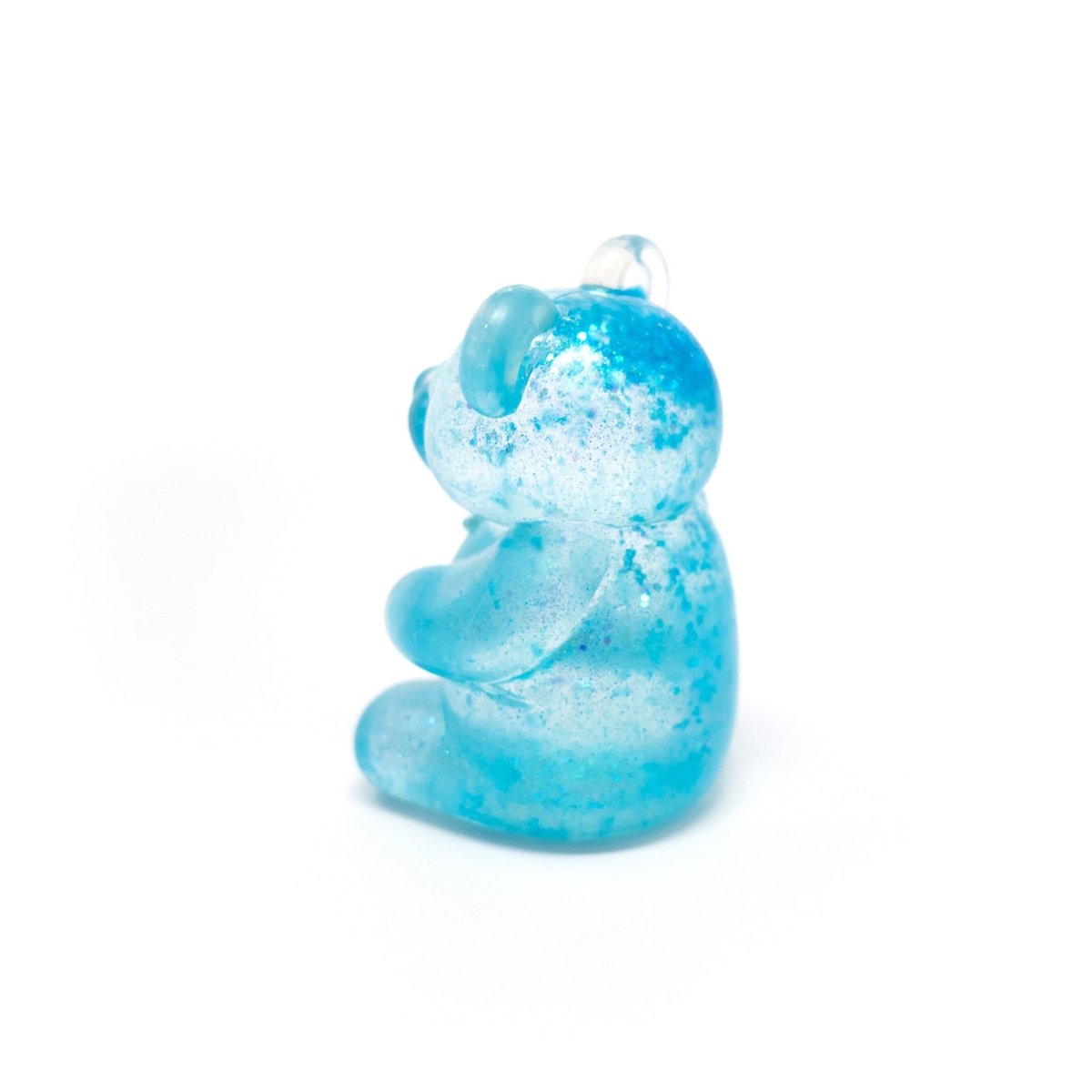 A small, translucent blue bear-shaped pendant from Bubblegum’s Favorite Toy - Glitter Maltose Bears, reminiscent of a glitter bear sensory toy, is photographed against a white background. The upright bear is viewed from a slight side angle.