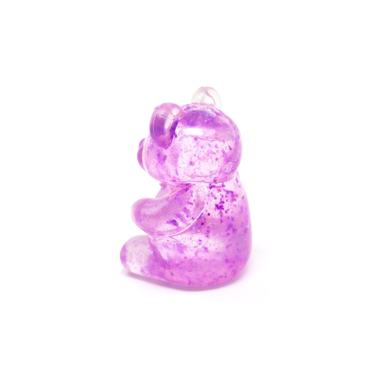 A translucent purple gummy bear-shaped charm with glitter flecks sits upright on a white background, making Bubblegum’s Favorite Toy - Glitter Maltose Bears a delightful sensory toy perfect for squishy stress relief.