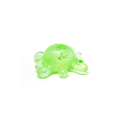 A small, green, semi-transparent blob with round protrusions sits on a white background, resembling a stylized germ or molecule. Perfect as a sensory toy or stress relief squishy, this delightful figure is inspired by Bubblegum’s Favorite Toy - Splat Squishy.