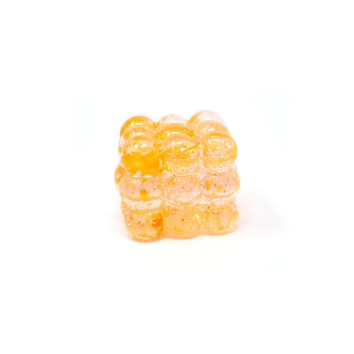 A small, translucent orange Glitter Bubble Cube from Bubblegum’s Favorite Toy, shaped like a cluster of bubbles, is shown on a white background.