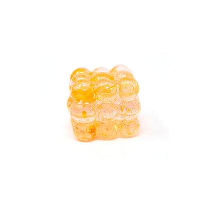 A small, translucent orange Glitter Bubble Cube from Bubblegum’s Favorite Toy, shaped like a cluster of bubbles, is shown on a white background.