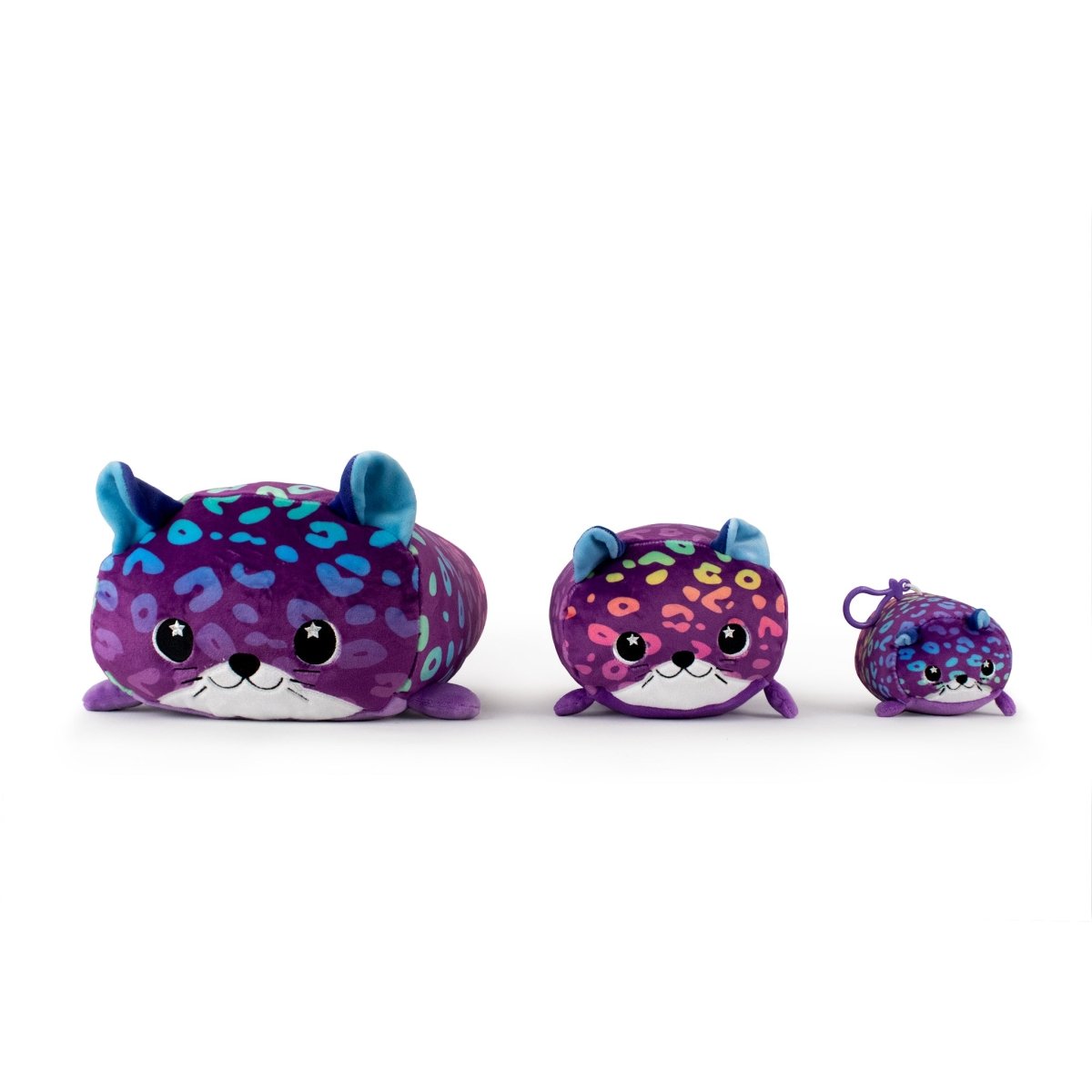 The Moosh-Moosh Series 5 includes three purple and blue leopard plushies of different sizes. The largest has a broad smile, the middle one is slightly smaller, and the smallest is Rayn the Leopard Plush Clip-On. All feature round eyes, small ears, and are set against a white background.