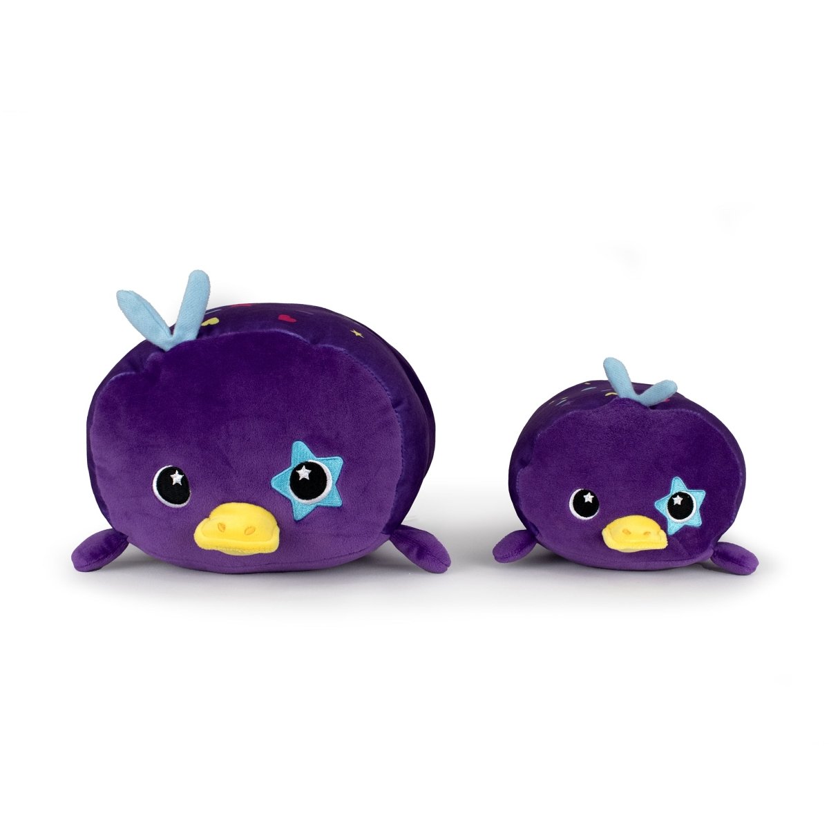 Two Sylvie the Platypus plushies—round, purple, with yellow beaks, blue star patches on their cheeks, and tiny blue wings on top—sit side by side against a white background, making perfect cozy cuddle buddies.