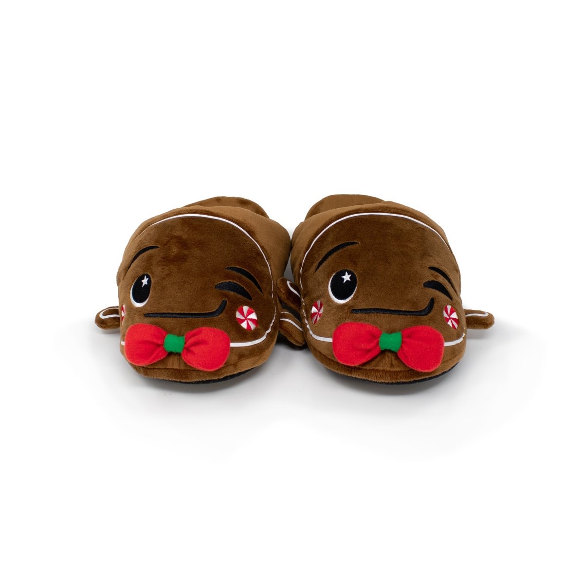 Gingersnaps the Gingerbread Slippers are cozy brown plush slippers resembling gingerbread men, featuring red bows, candy cane embellishments, and embroidered smiling faces against a white background.