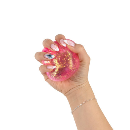 A hand with manicured nails, featuring a floral design, squeezes the pink Bubblegum's Favorite Toy - Glitter Sugah-mals Cube stress relief toy against a white background.