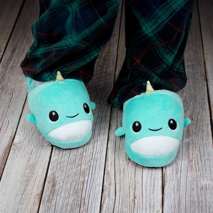 A child wears Chunky Monkey Kids Slipper with smiling faces, little horns, star-shaped eyes, and non-slip soles alongside dark plaid pajama pants on a wooden floor—perfect for cozy comfort at home.