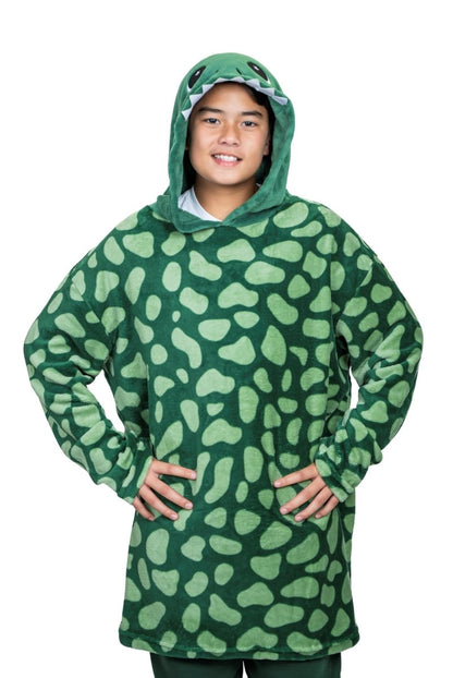 A person showcases the Dinosaur Hooded Blanket, which resembles a soft stuffed animal. The green ensemble features cartoon eyes on the hood and a spotted pattern, standing with hands on hips against a white background.