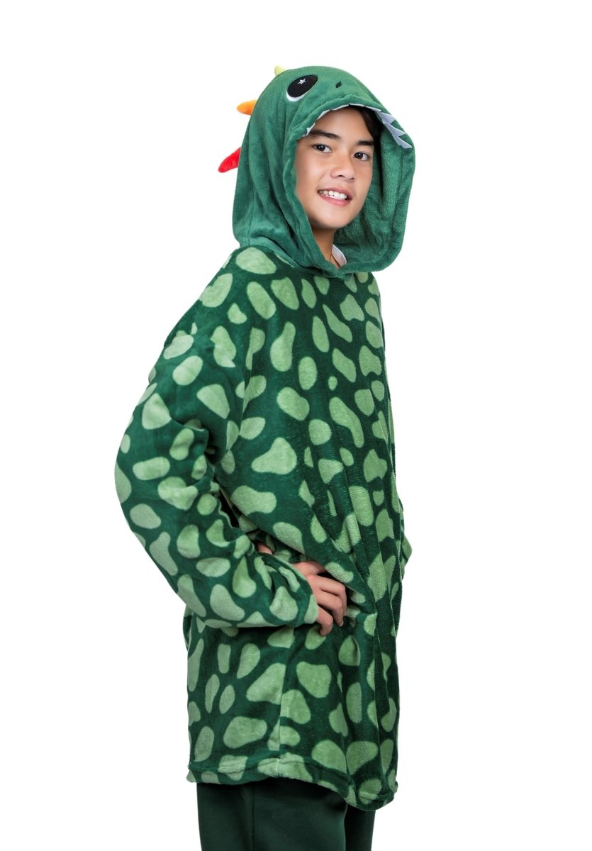 A person wearing a Dinosaur Hooded Blanket with a green dinosaur theme, featuring eyes and teeth on the hood, resembles a playful plushie costume. The soft, spotted fabric enhances the whimsical look as they smile with hands on hips against a white background.