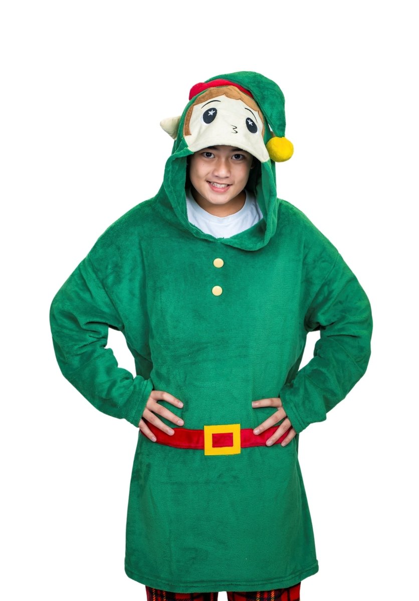 A person dressed in a green Jingle the Elf Hooded Blanket with a red belt, yellow buttons, and cartoonish animal-like hood and ears. The ensemble is paired with red plaid pants. They're smiling with hands on hips against a white background.