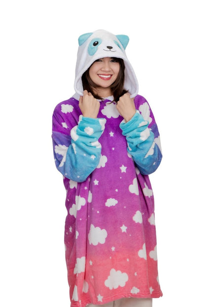 Smiling, a person is wrapped in the Panda Hooded Blanket featuring a cute panda design. This cozy blend of purple and pink displays white clouds and stars. Its hood, with blue ears and a panda face, resembles a plushie against a pristine white background.