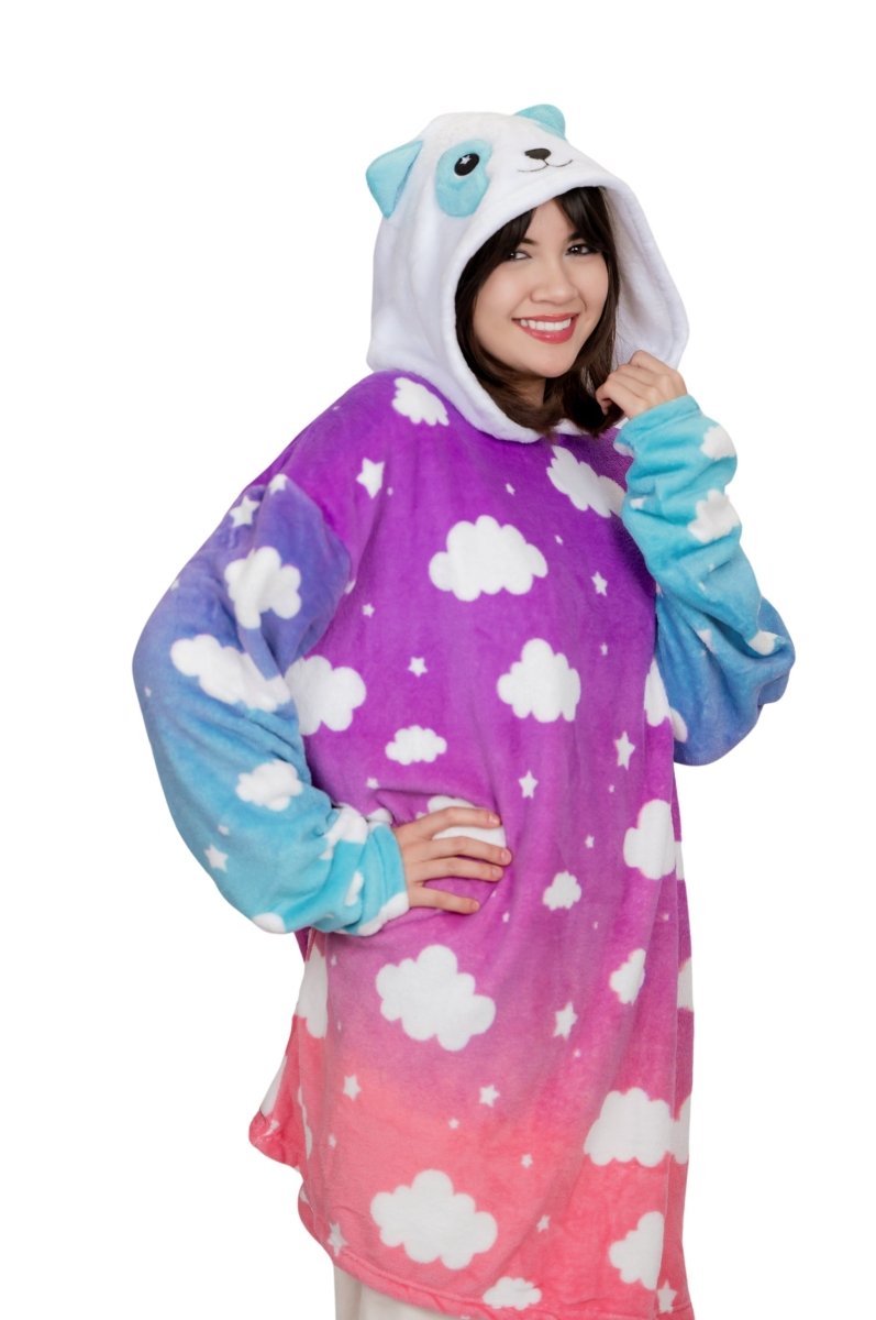 A person in a cute, colorful "Panda Hooded Blanket," featuring an oversized design with a panda face on the hood. The blanket showcases a plushie-like gradient from purple to pink, adorned with white clouds and stars. The person smiles, one hand on their hip and the other holding the hood.