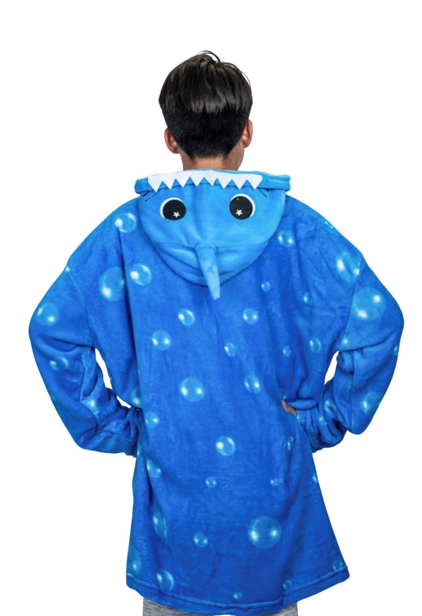 A person in a blue oversized Shark Hooded Blanket featuring bubble patterns and a cartoon face on the hood stands with hands on hips, exuding plush toy coziness while facing away from the camera.