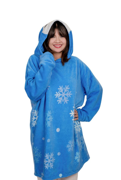 A smiling person wears the Peckington the Penguin Hooded Blanket, a cozy blue fleece with white snowflakes and dots—perfect as a holiday gift.