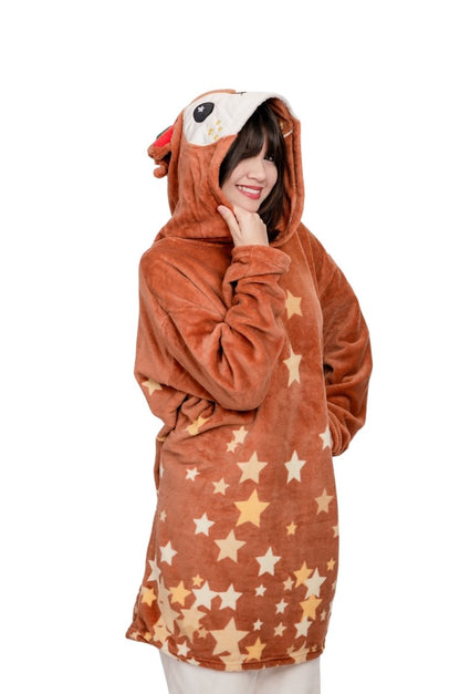 A person wears the Mitzy the Reindeer Hooded Blanket, featuring a cute cartoon reindeer face on the hood and a star-patterned brown body, smiling and posing against a white background.