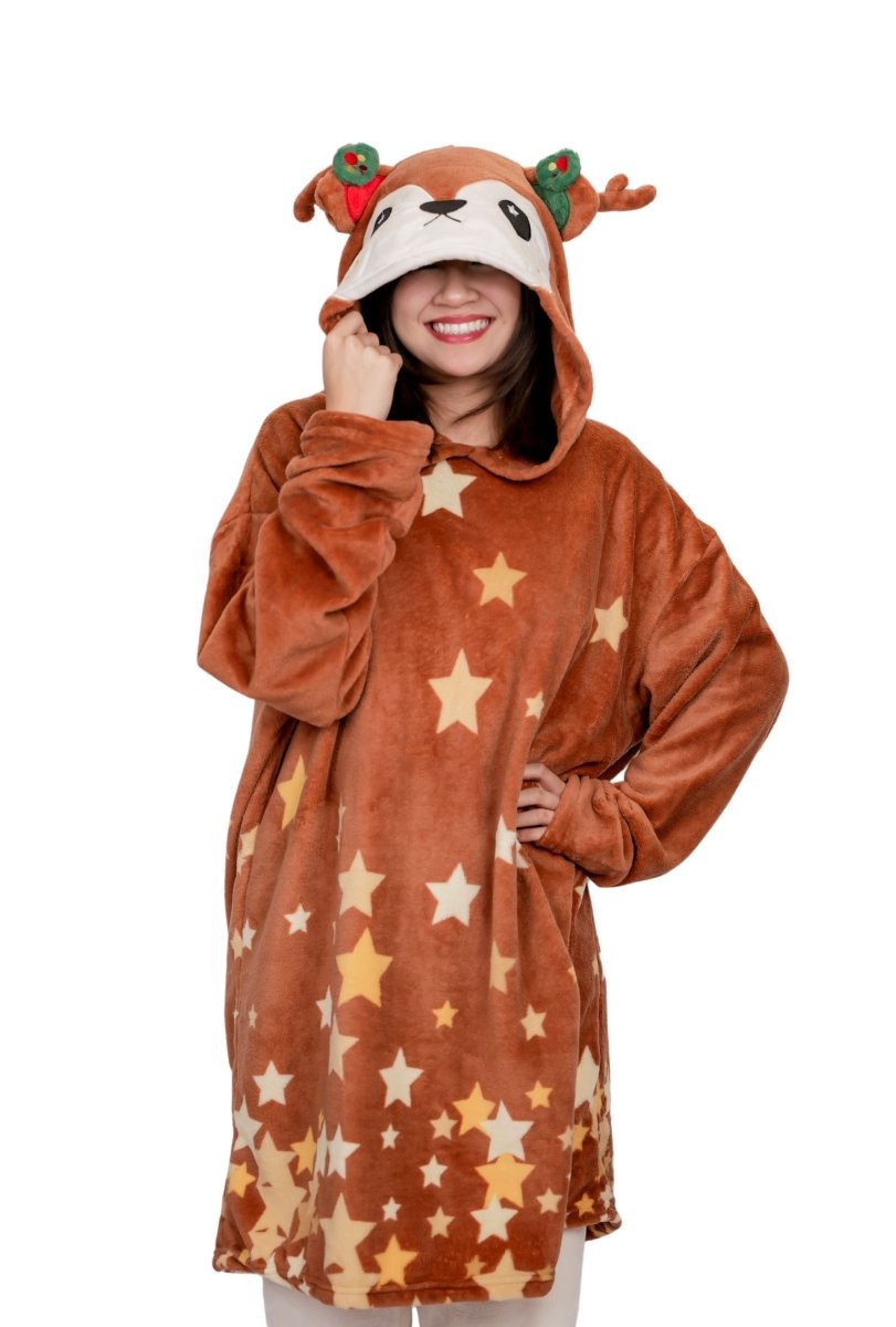 A person smiles in the Mitzy the Reindeer Hooded Blanket, featuring a reindeer face, antlers, red decorations, and star patterns. The hood is up against a plain white background for a festive holiday look.