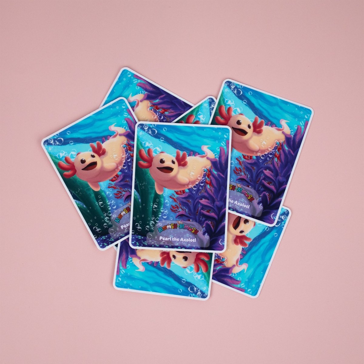 Seven vibrant Moosh-Moosh 3" x 4" vinyl stickers show a smiling cartoon axolotl underwater with plants and bubbles, scattered on a pink surface.