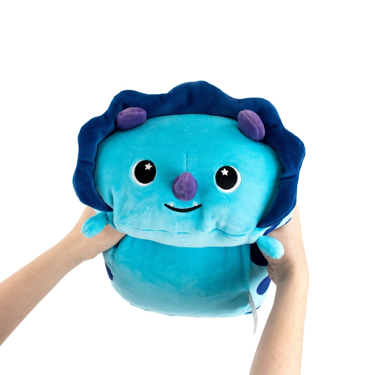 Hands are holding up a light blue plush toy with a smiling face, big eyes, and dark blue frilled edges like a jellyfish. It has purple spots and small appendages. This charming toy might rival Dina the Dinosaur in appeal. The background is white.