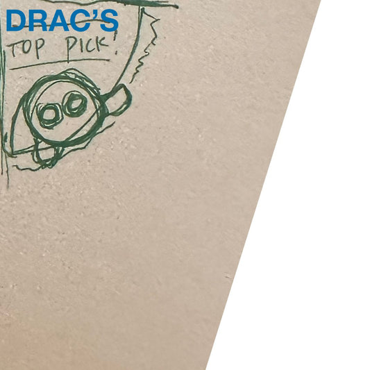 A hand-drawn cartoon character with big round eyes and arms stands on a textured surface beside torn paper reading "TOP PICK!" and the product name "Drac's Favorite Toy" in blue at the top left corner.